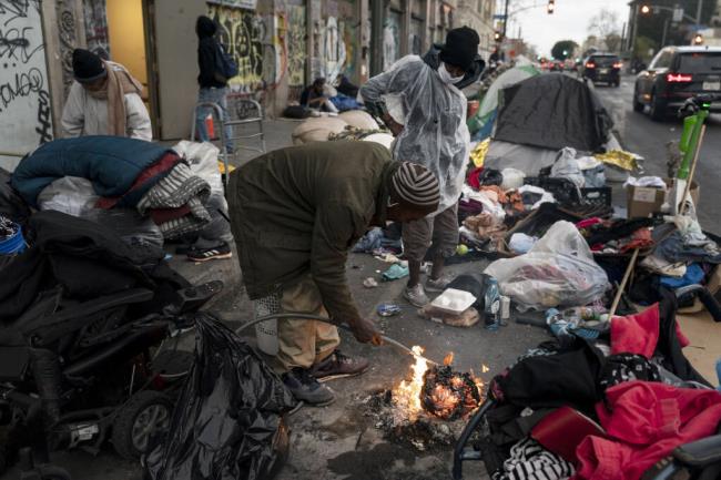 FILE - Robert Mason, a 56-year-old homeless man, warms up a piece of doughnut over a bo<em></em>nfire he set to keep himself warm on Skid Row in Los Angeles, on Feb. 14, 2023. (AP Photo/Jae C. Hong, File)